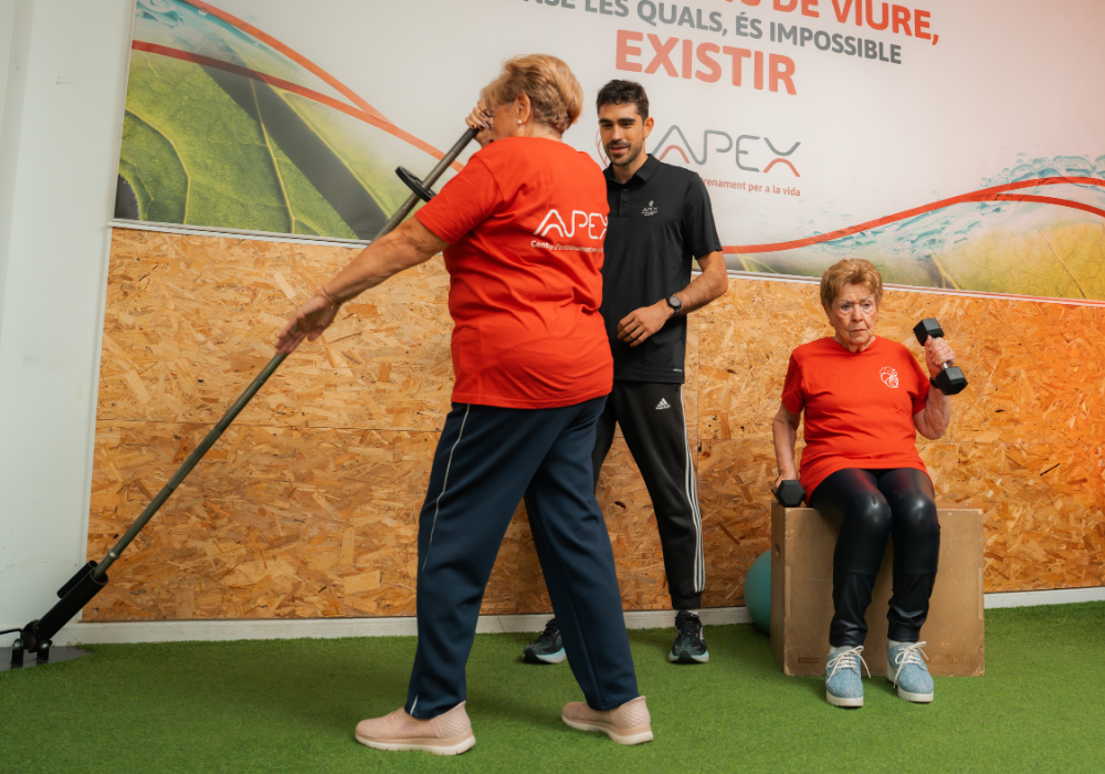 Entrenamiento multicomponente para tercera edad-apex-benifayo Entrenador personal supervisando técnica de ejercicio con barra landmine y mancuernas de mujeres senior en el gimnasio.