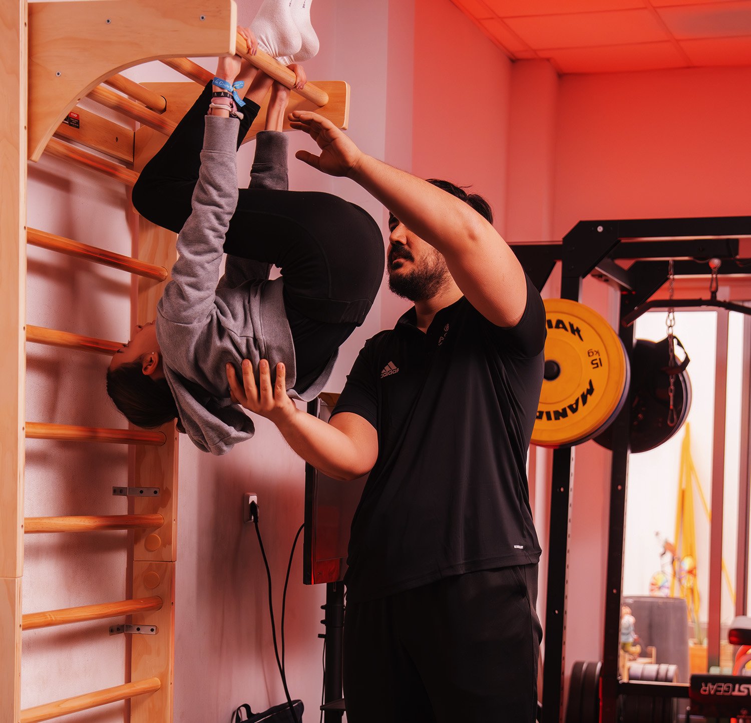 benifaio deporte adaptado Entrenador personal supervisando técnica de ejercicio de movilidad en espaldera de una joven en el gimnasio.