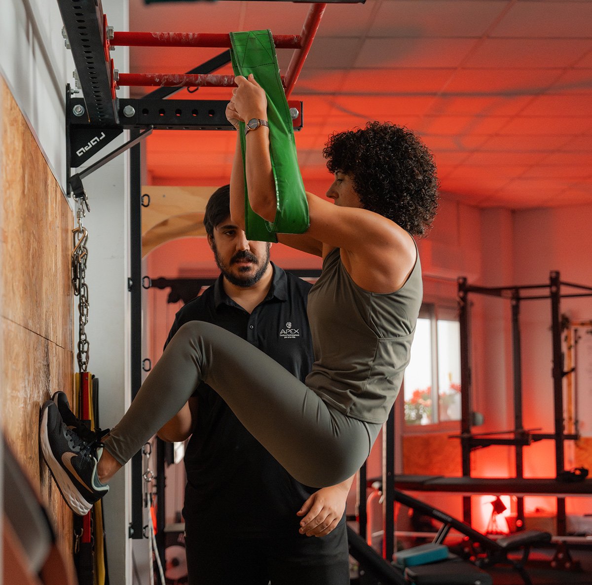 benifaio gimnasio Entrenador personal supervisando técnica de elevación de rodillas en barra con correas de una mujer en el gimnasio.