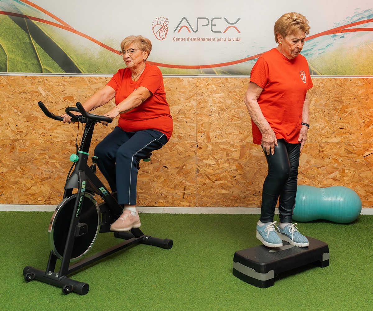Mujeres senior realizando ejercicios de cardio con bicicleta estática y step en el gimnasio.
