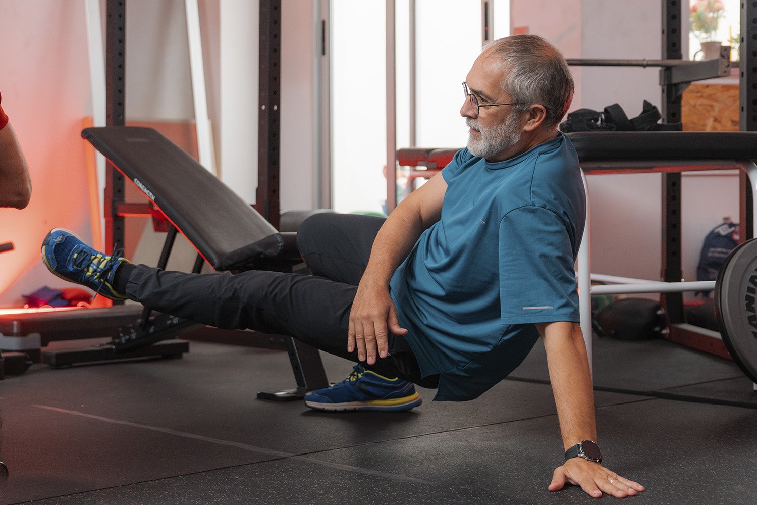 Ejercicio de movilidad y fuerza en suelo de un cliente senior en el gimnasio.