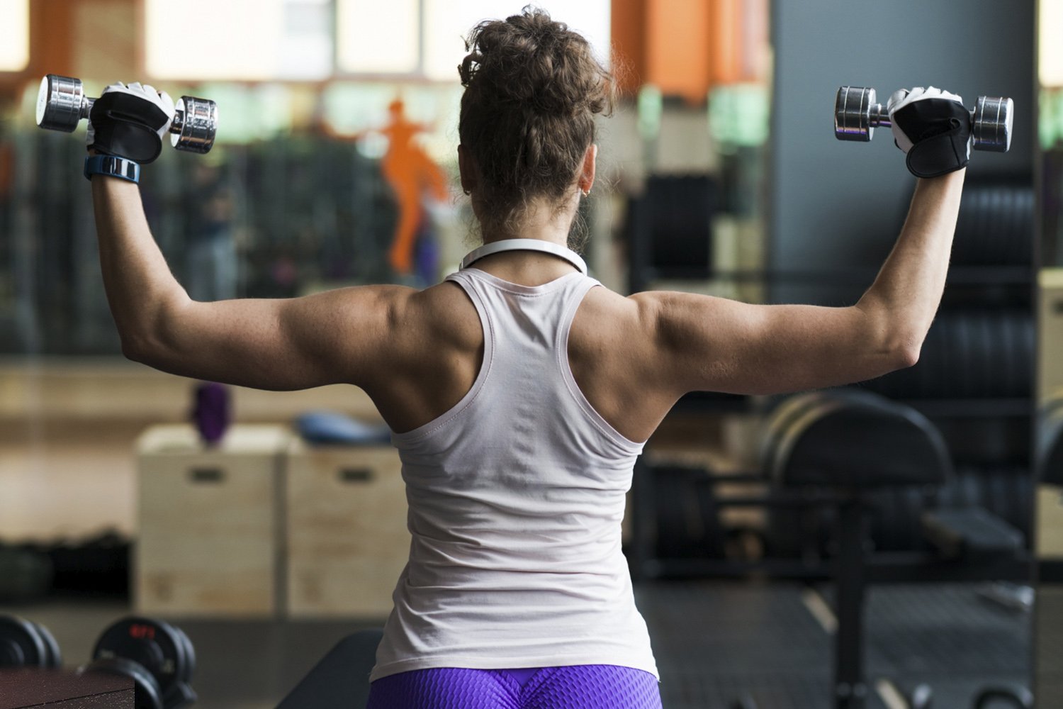 Mujer entrenando espalda y hombros con mancuernas.
