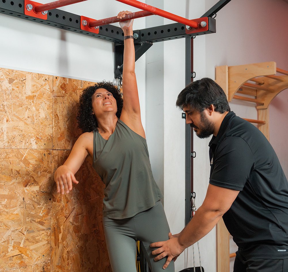 Entrenador personal supervisando técnica de estiramiento y movilidad en barra de una mujer en el gimnasio.