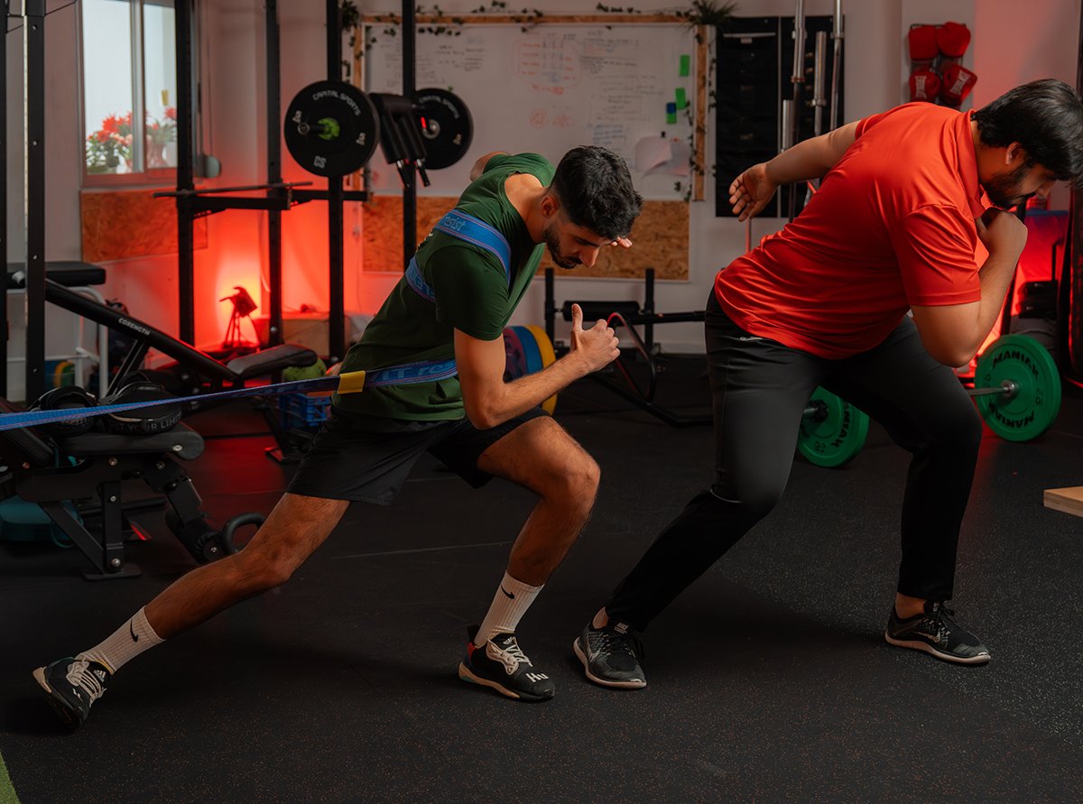 entrenamiento personalizado benifaio Entrenador personal supervisando técnica de carrera con banda de resistencia de un joven en el gimnasio.