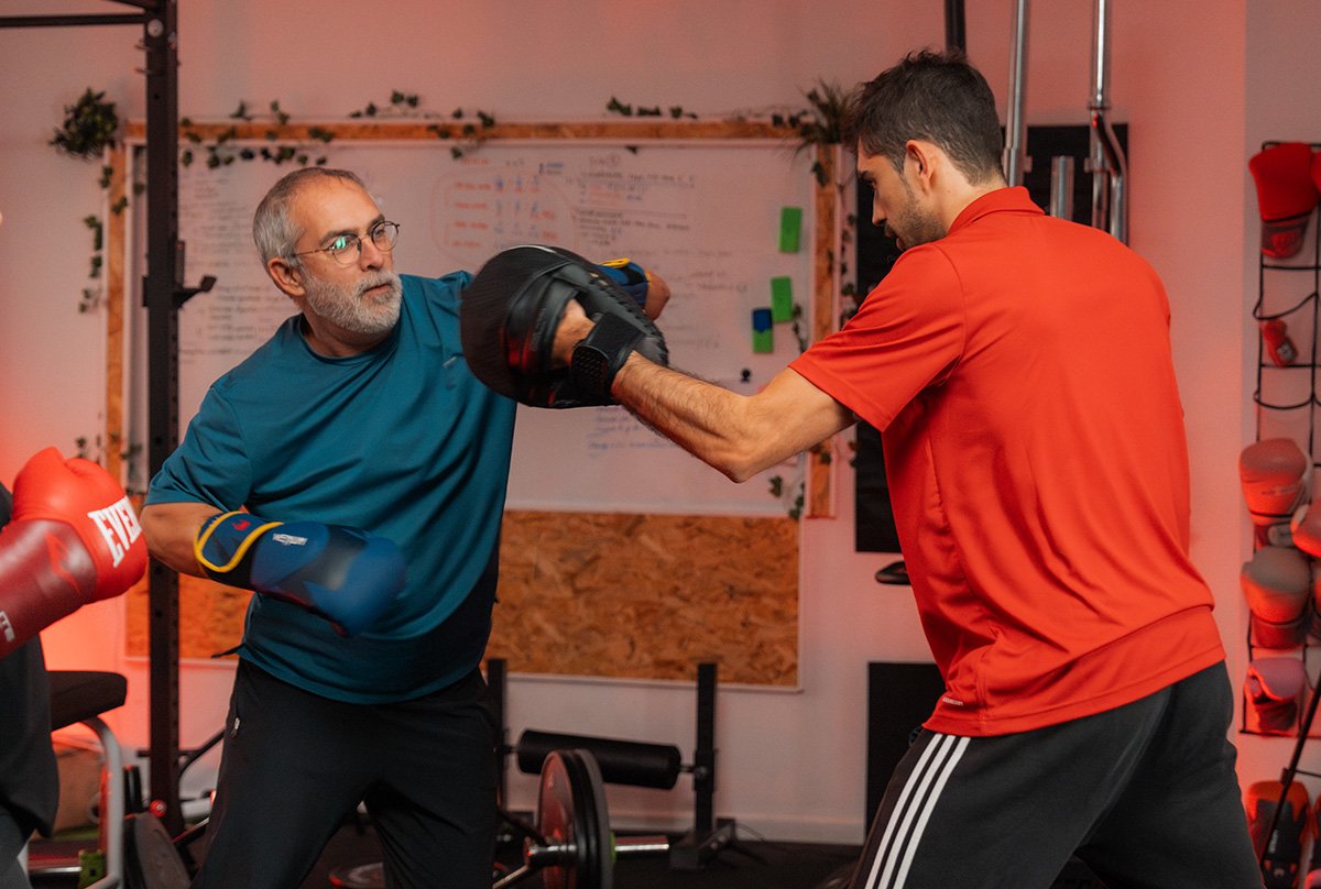entrenar benifaio Entrenador personal supervisando técnica de golpeo de boxeo con manoplas de un cliente senior en el gimnasio.