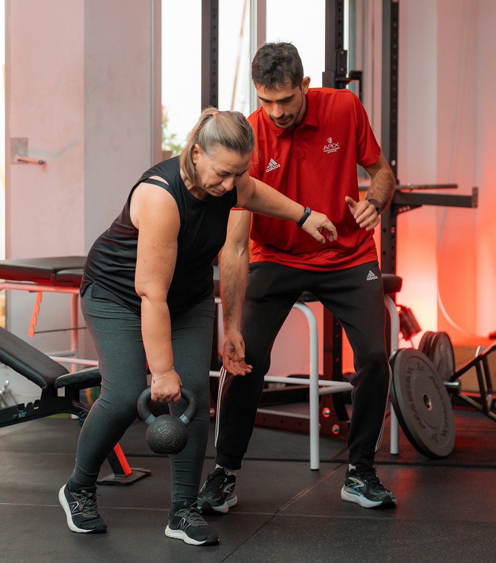 menopausia entrenamiento Entrenador personal supervisando técnica de peso muerto rumano con kettlebell de una mujer senior en el gimnasio.