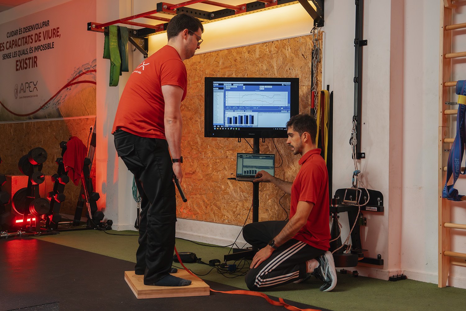 Entrenador personal supervisando técnica de ejercicio de fuerza en plataforma de medición de un joven en el gimnasio.